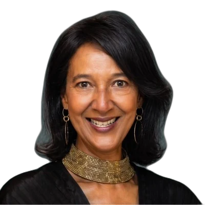 A smiling middle-aged woman with shoulder-length dark hair. She wears a wide, textured gold choker necklace and simple gold hoop earrings with a dark top.